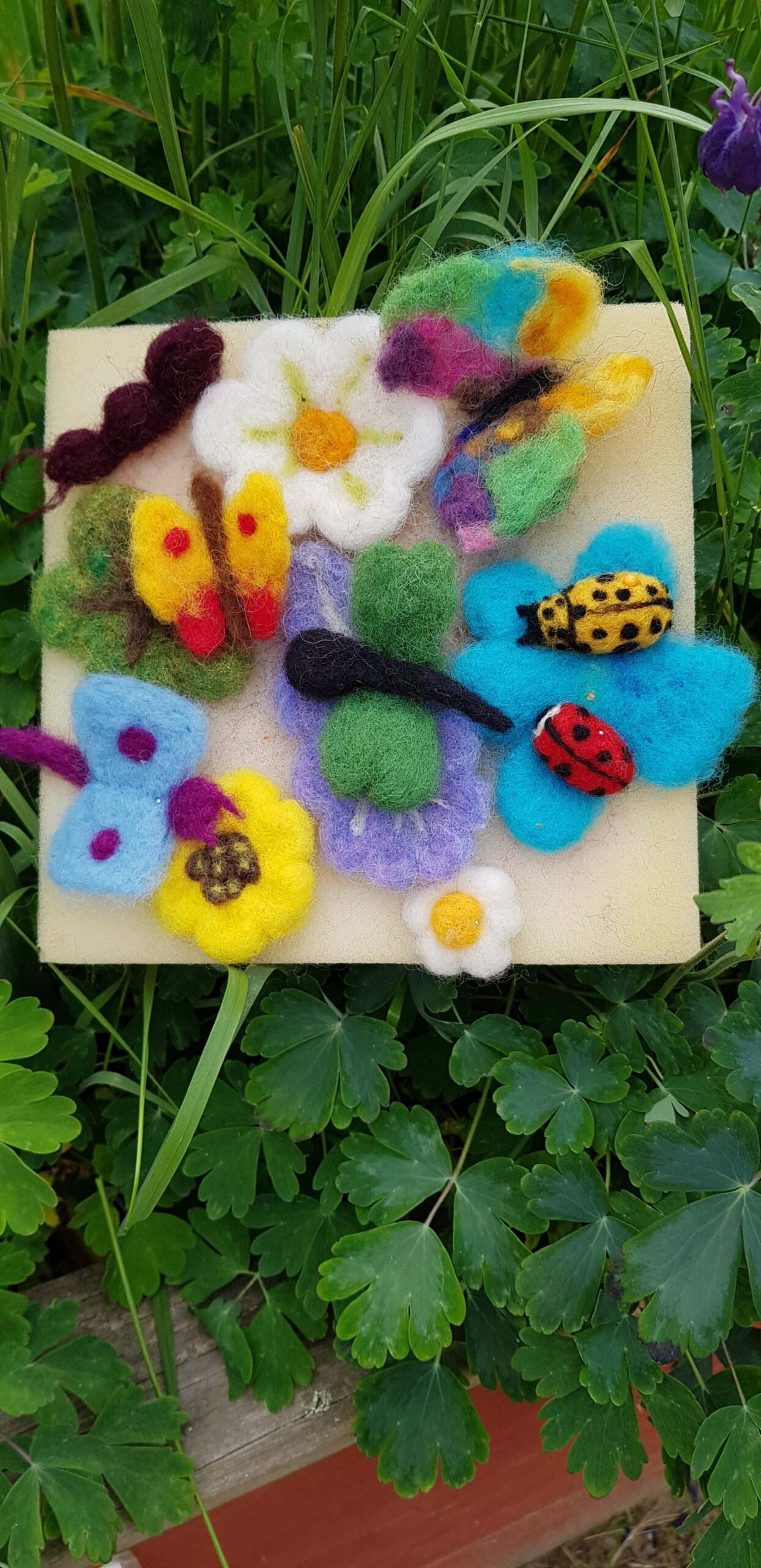 Färgglada blommor, fjärilar och nyckelpigor i tovad ull.